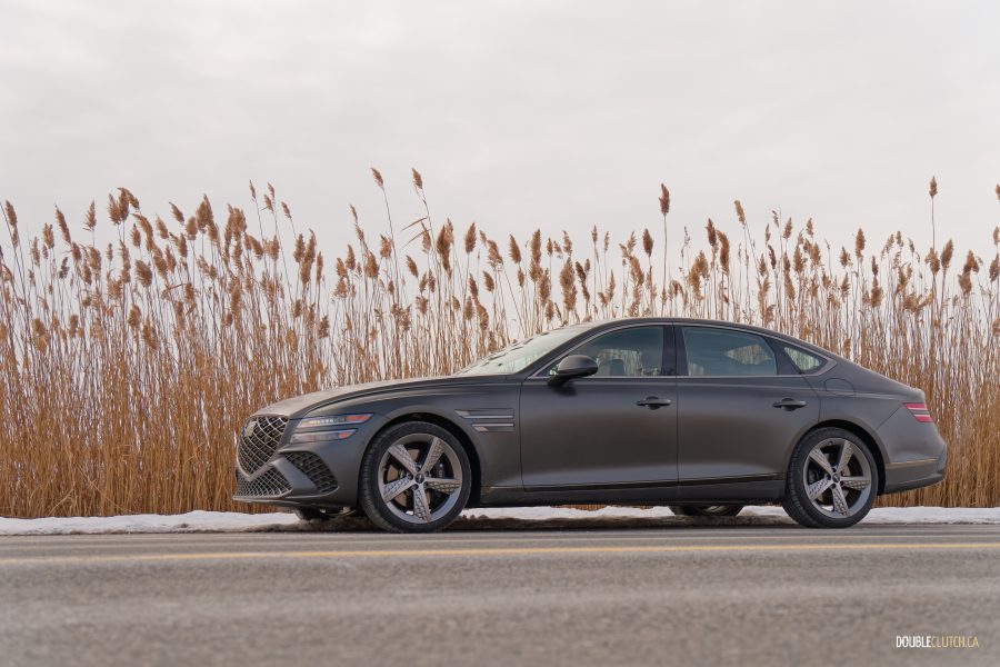 Front quarter view of a 2025 Genesis G80 3.5T Sport in a snowy parking lot with trees in the background