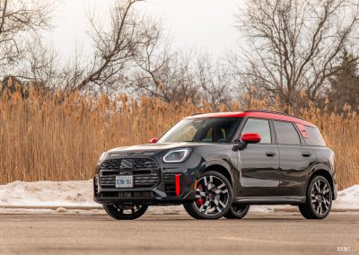 Front quarter view of a 2025 Mini Countryman JCW in a parking lot with trees and shrubs in the background