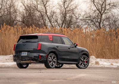 Rear quarter view of a 2025 Mini Countryman JCW in a parking lot with trees and shrubs in the background