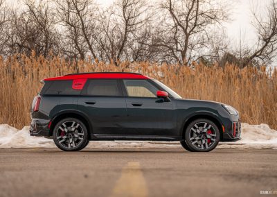 Side profile view of a 2025 Mini Countryman JCW in a parking lot with trees and shrubs in the background