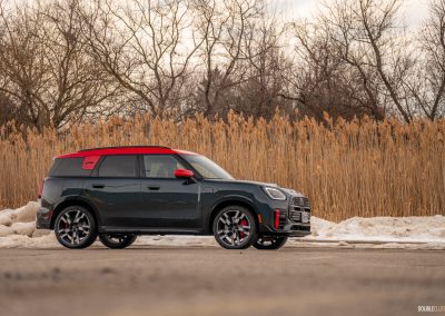 Front angle view of a 2025 Mini Countryman JCW in a parking lot with trees and shrubs in the background