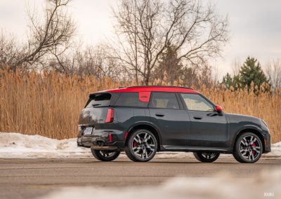 Rear angle view of a 2025 Mini Countryman JCW in a parking lot with trees and shrubs in the background
