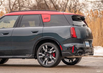 Rear quarter view of a 2025 Mini Countryman JCW in a parking lot with trees and shrubs in the background