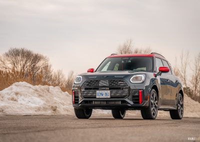 Front quarter view of a 2025 Mini Countryman JCW in a parking lot with trees and shrubs in the background