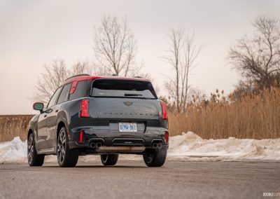Rear quarter view of a 2025 Mini Countryman JCW in a parking lot with trees and shrubs in the background