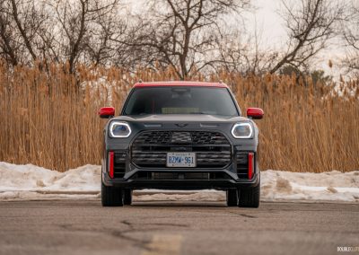 Front view of a 2025 Mini Countryman JCW in a parking lot with trees and shrubs in the background