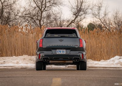 Rear view of a 2025 Mini Countryman JCW in a parking lot with trees and shrubs in the background