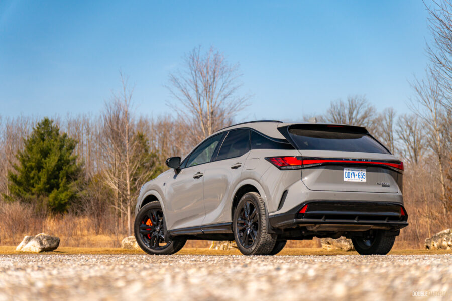 Rear quarter view of a grey 2025 Lexus RX 500h Black Line Special Edition on a sunny day with trees in the background