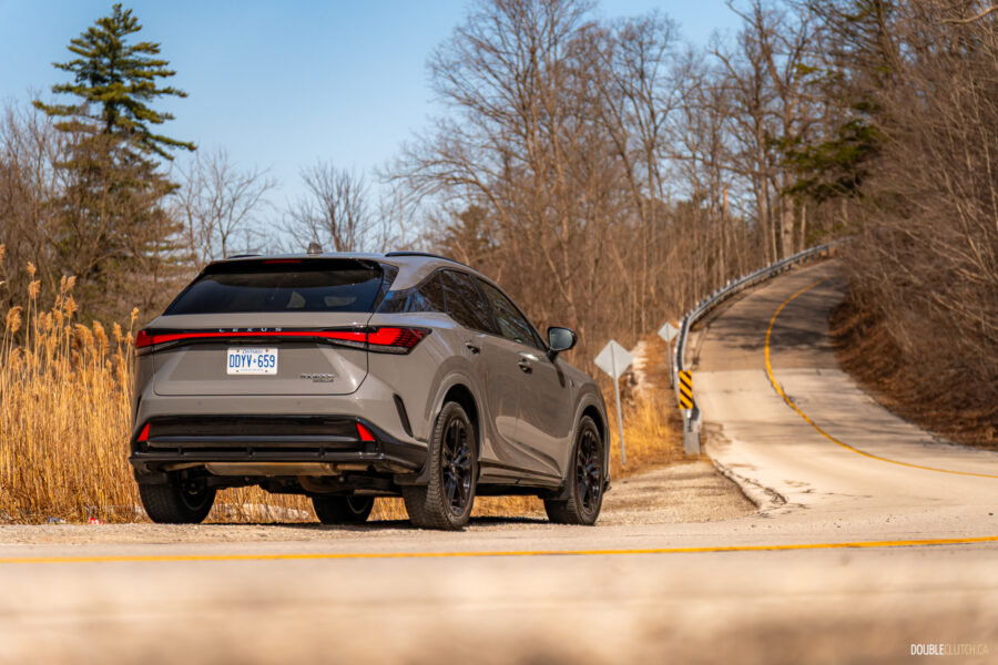 Rear quarter view of a grey 2025 Lexus RX 500h Black Line Special Edition on a sunny day with trees in the background