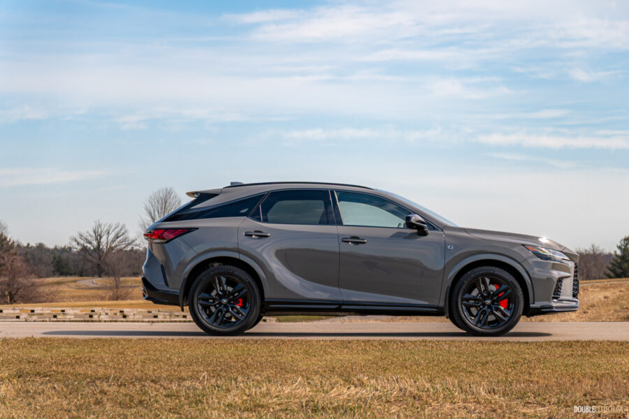Side profile view of a grey 2025 Lexus RX 500h Black Line Special Edition on a sunny day with trees in the background