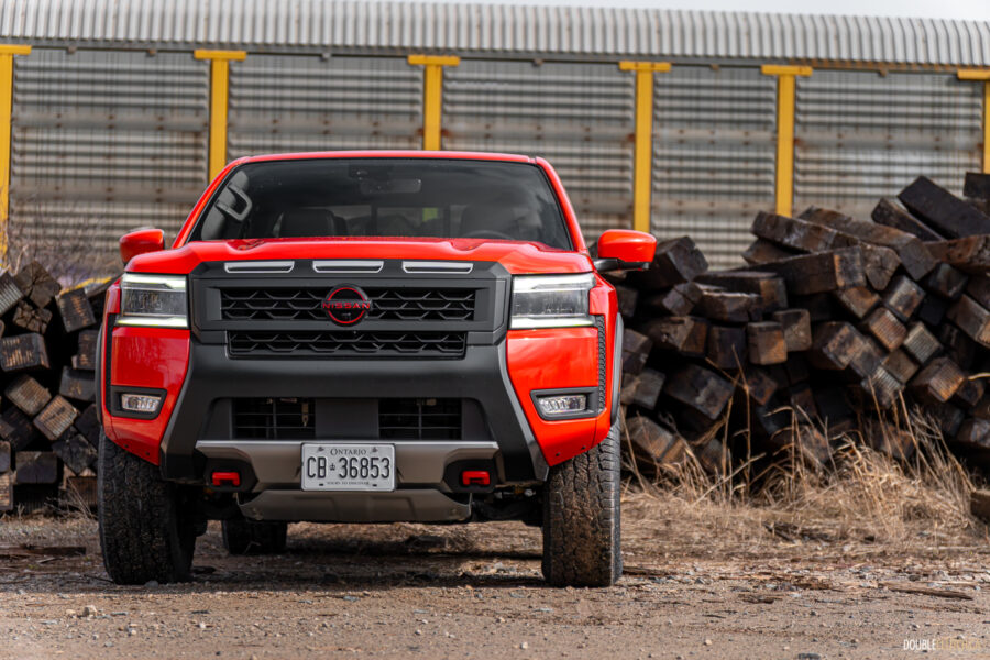 Front view of an orange 2025 Nissan Frontier PRO-4X Luxury on a cloudy day, with trees and a train in the background