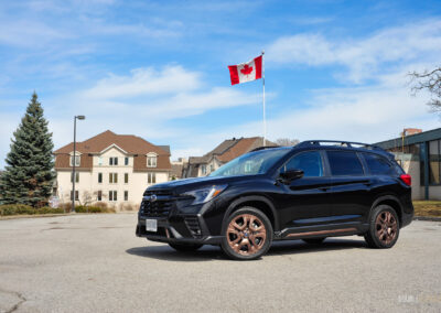 Front quarter view of a black 2025 Subaru Ascent on a sunny day, with houses and the Canadian flag in the background