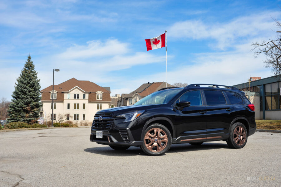 Front quarter view of a black 2025 Subaru Ascent on a sunny day, with houses and the Canadian flag in the background