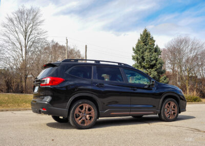 Rear quarter view of a black 2025 Subaru Ascent on a sunny day, with trees in the background