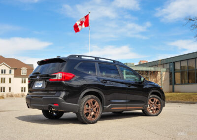 Rear quarter view of a black 2025 Subaru Ascent on a sunny day, with houses and the Canadian flag in the background