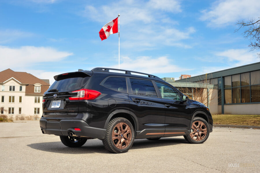Rear quarter view of a black 2025 Subaru Ascent on a sunny day, with houses and the Canadian flag in the background