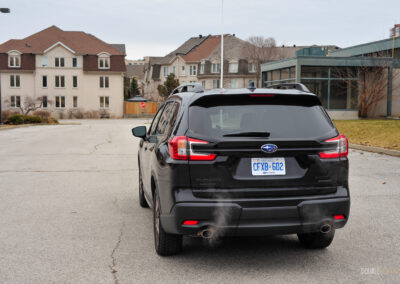 Rear quarter view of a black 2025 Subaru Ascent on a cloudy day, with trees and houses in the background