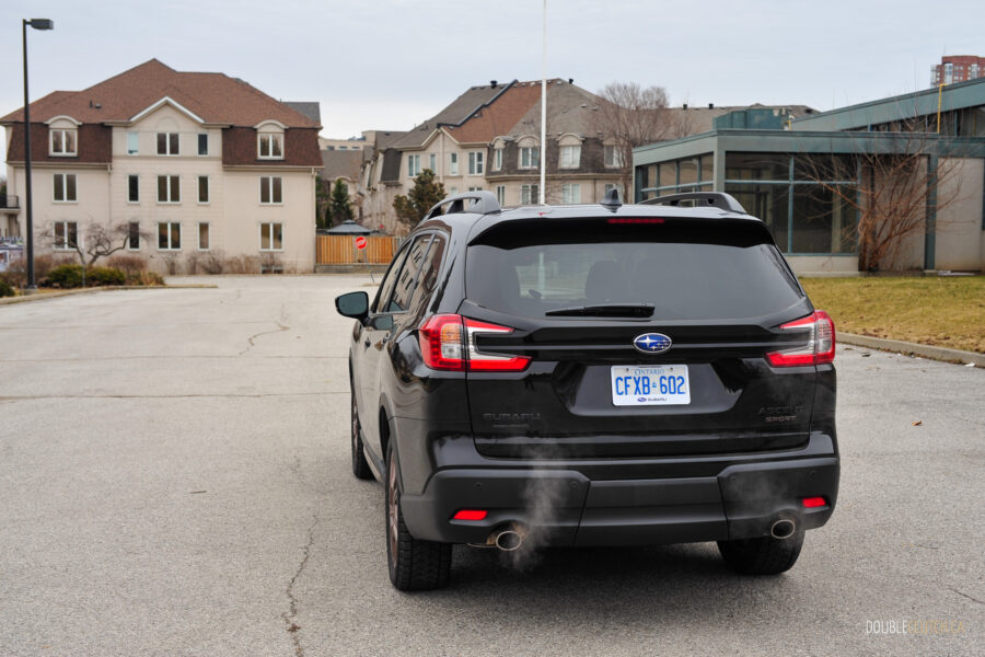Rear quarter view of a black 2025 Subaru Ascent on a cloudy day, with trees and houses in the background