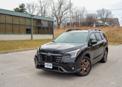 Front quarter view of a black 2025 Subaru Ascent on a cloudy day, with trees and houses in the background