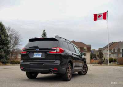 Rear quarter view of a black 2025 Subaru Ascent on a cloudy day, with trees and houses in the background