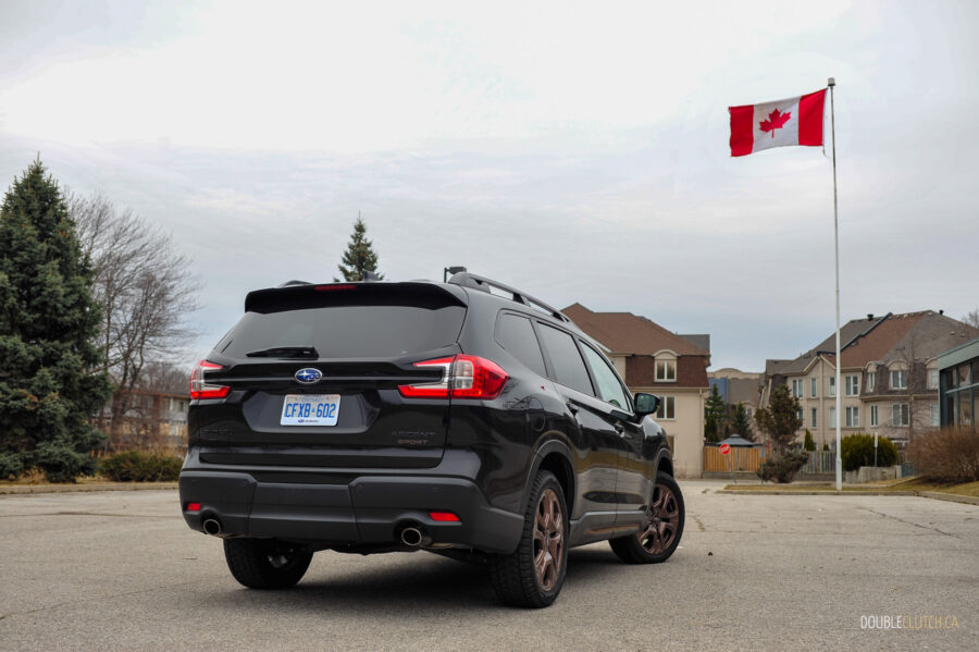 Rear quarter view of a black 2025 Subaru Ascent on a cloudy day, with trees and houses in the background