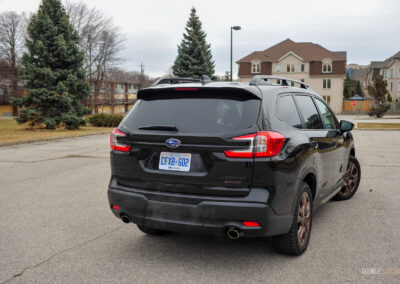 Rear quarter view of a black 2025 Subaru Ascent on a cloudy day, with trees and houses in the background