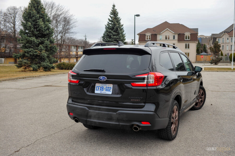 Rear quarter view of a black 2025 Subaru Ascent on a cloudy day, with trees and houses in the background