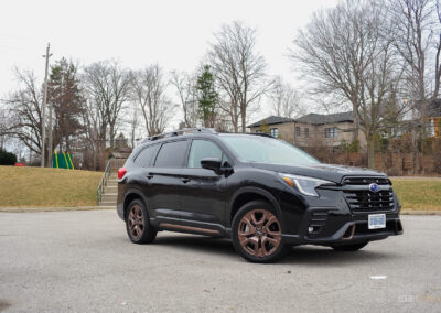 Front quarter view of a black 2025 Subaru Ascent on a cloudy day, with trees and houses in the background
