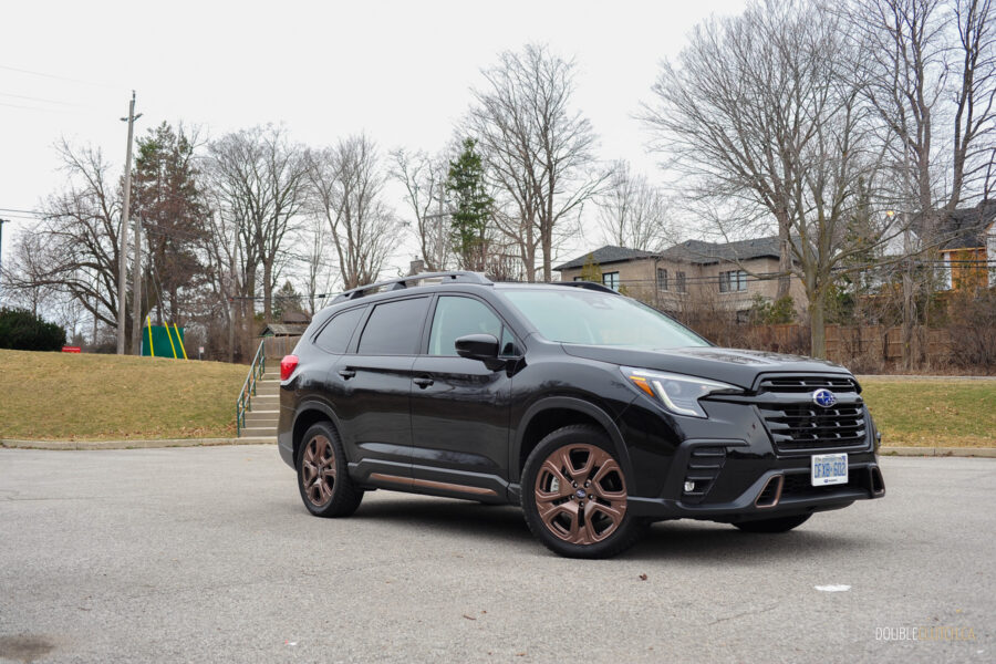 Front quarter view of a black 2025 Subaru Ascent on a cloudy day, with trees and houses in the background