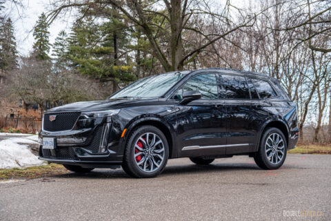 Front quarter view of a black 2025 Cadillac XT6 on a cloudy day, with trees in the background