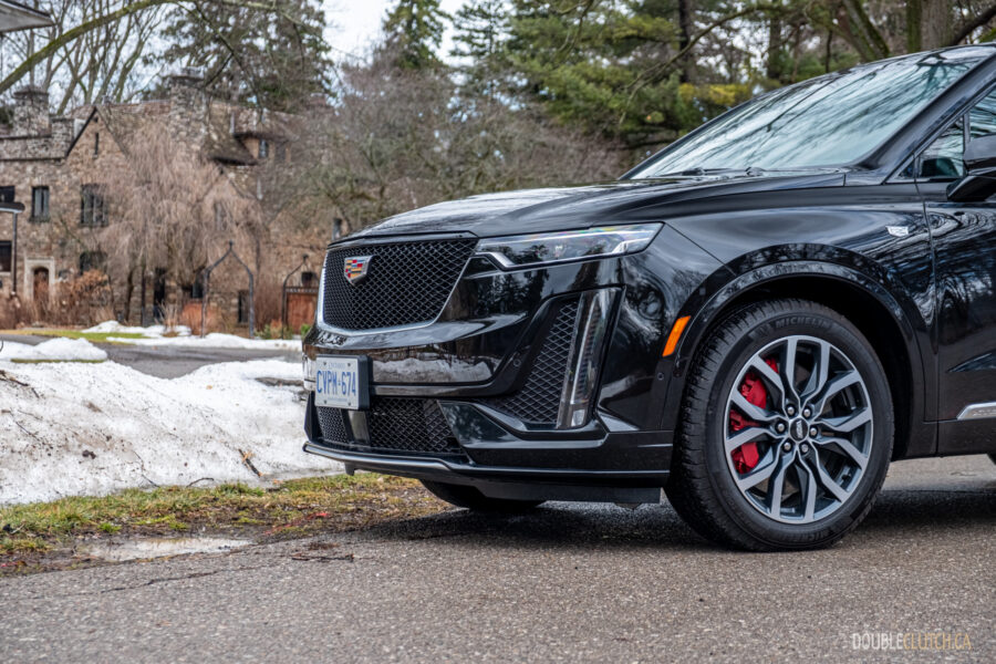 Front quarter view of a black 2025 Cadillac XT6 on a cloudy day, with trees in the background