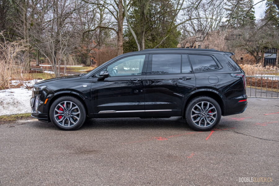Side profile view of a black 2025 Cadillac XT6 on a cloudy day, with trees in the background