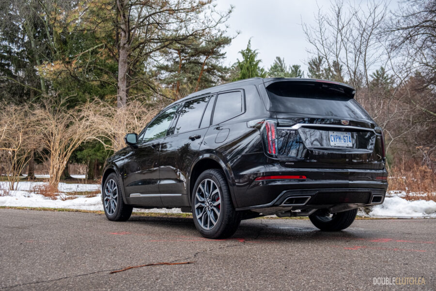 Rear quarter view of a black 2025 Cadillac XT6 on a cloudy day, with trees in the background