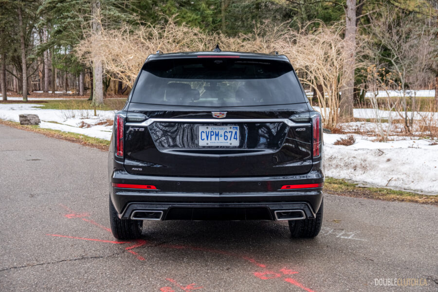 Rear view of a black 2025 Cadillac XT6 on a cloudy day, with trees in the background
