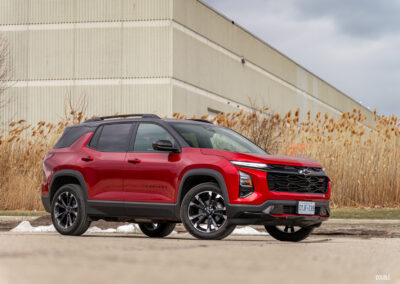 Front quarter view of a red 2025 Chevrolet Equinox RS with a building and shrubs in the background