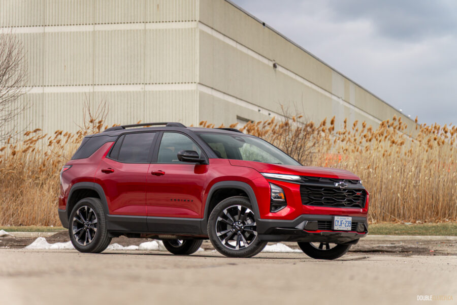 Front quarter view of a red 2025 Chevrolet Equinox RS with a building and shrubs in the background