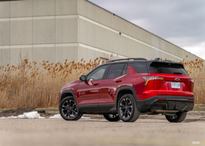 Rear quarter view of a red 2025 Chevrolet Equinox RS with a building and shrubs in the background