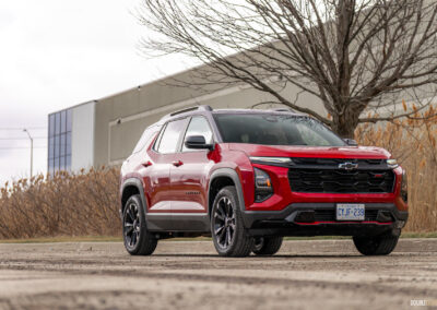 Front quarter view of a red 2025 Chevrolet Equinox RS with a building and shrubs in the background