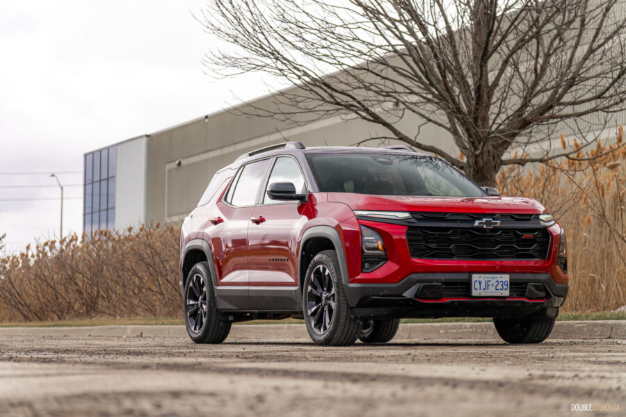 Front quarter view of a red 2025 Chevrolet Equinox RS with a building and shrubs in the background