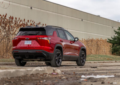 Rear quarter view of a red 2025 Chevrolet Equinox RS with a building and shrubs in the background