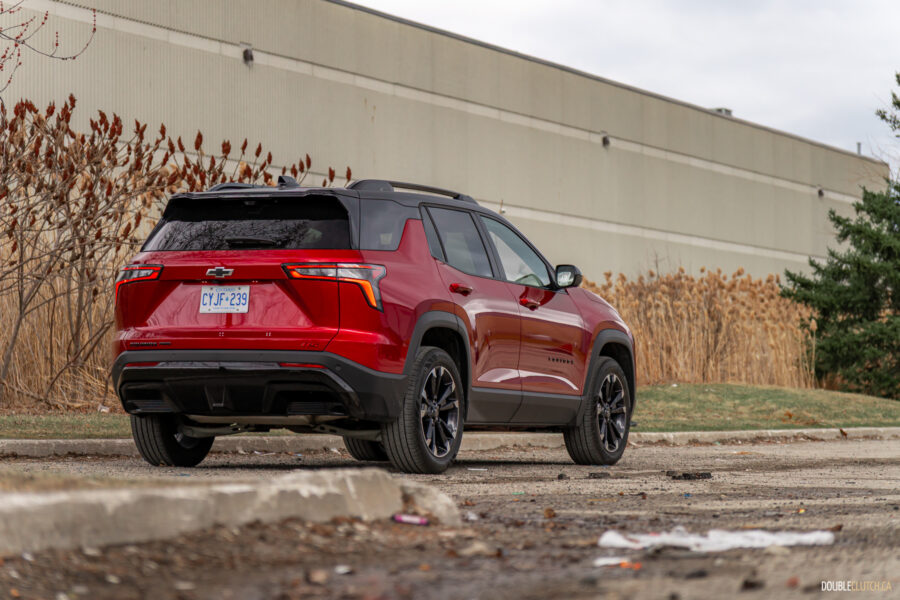 Rear quarter view of a red 2025 Chevrolet Equinox RS with a building and shrubs in the background