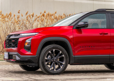 Front quarter view of a red 2025 Chevrolet Equinox RS with a building and shrubs in the background