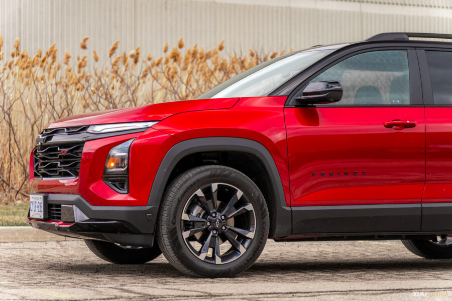 Front quarter view of a red 2025 Chevrolet Equinox RS with a building and shrubs in the background