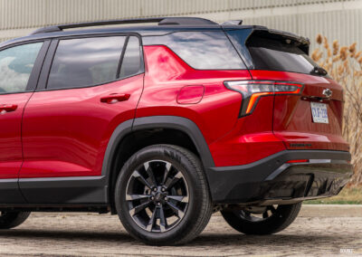 Rear quarter view of a red 2025 Chevrolet Equinox RS with a building and shrubs in the background