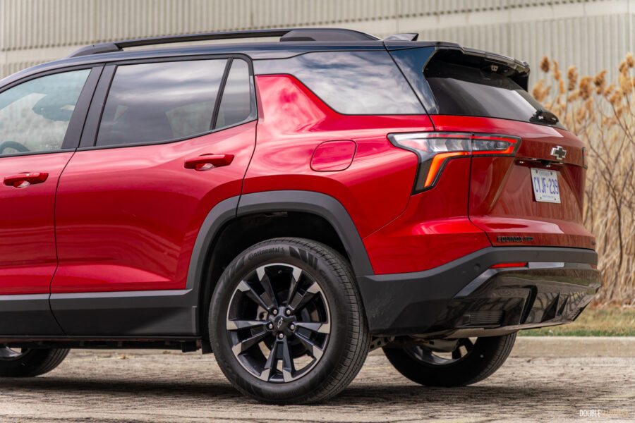Rear quarter view of a red 2025 Chevrolet Equinox RS with a building and shrubs in the background