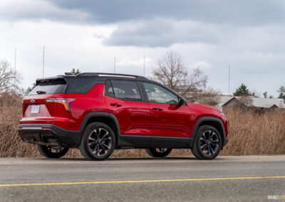 Rear quarter view of a red 2025 Chevrolet Equinox RS on a cloudy day with trees in the background