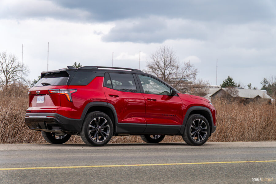 Rear quarter view of a red 2025 Chevrolet Equinox RS on a cloudy day with trees in the background
