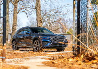 Front quarter view of a dark blue 2025 Genesis GV70 3.5T Sport Plus on a sunny day, with trees in the background
