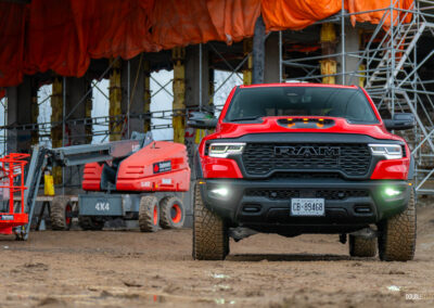 Front view of a red 2025 Ram 1500 RHO, parked in a muddy construction site