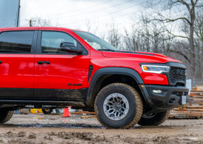 Cropped front quarter view of a red 2025 Ram 1500 RHO, showing the restyled front fascia and wheels, with trees in the background